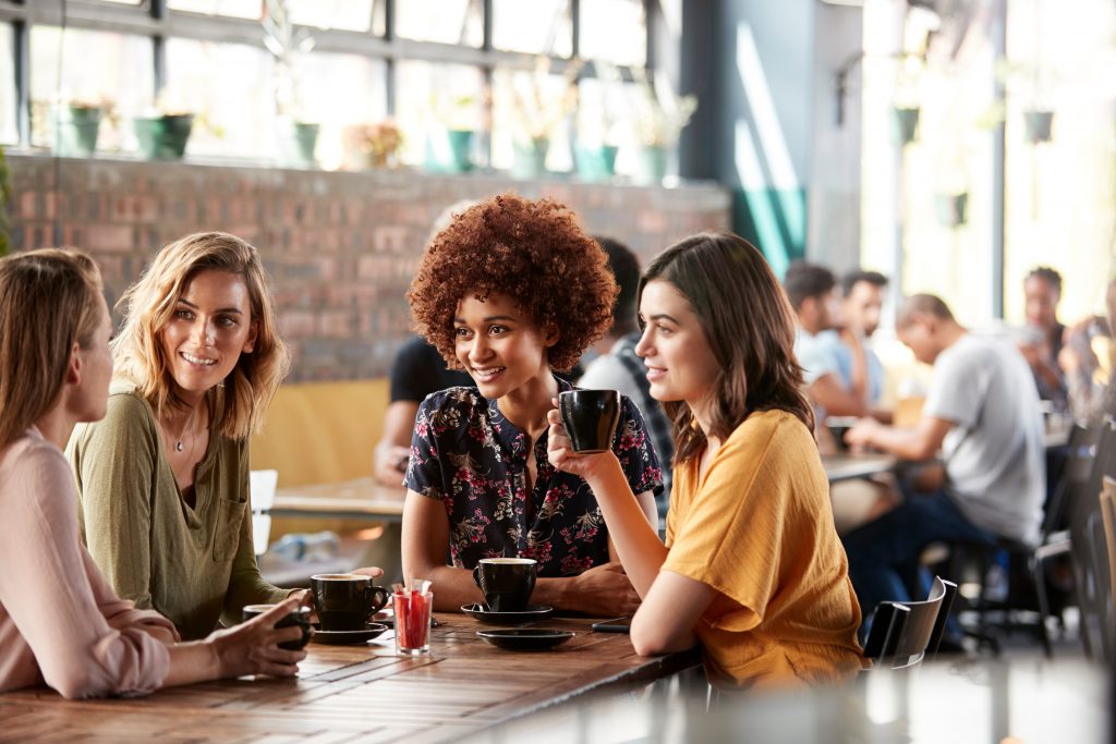 Four Young Female Friends Meeting Sit At Table In Coffee Shop And Talk - Networking tips for introverts
